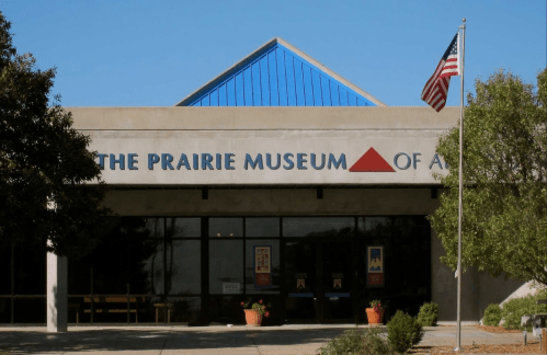 Exterior of the Prairie Museum of Art, featuring a blue roof, large windows, and an American flag.