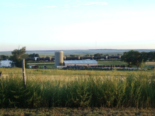 A rural landscape featuring a farm with a silo, hay bales, and fields under a clear sky.