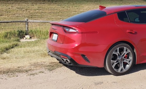 A red sports car parked on a dirt road near a grassy field and wooden fence.