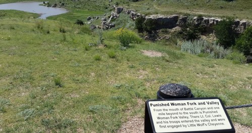 A scenic view of Punished Woman Fork and Valley, with a sign detailing its historical significance.