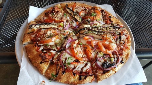 A delicious pizza topped with tomatoes, onions, and grilled vegetables on a crispy crust, served on a metal table.