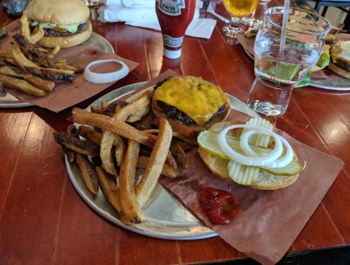 A plate with a cheeseburger, pickles, onions, fries, ketchup, and a glass of water on a wooden table.