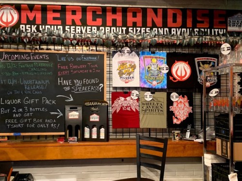 Merchandise display featuring T-shirts, event announcements, and a liquor gift pack at a bar or brewery.