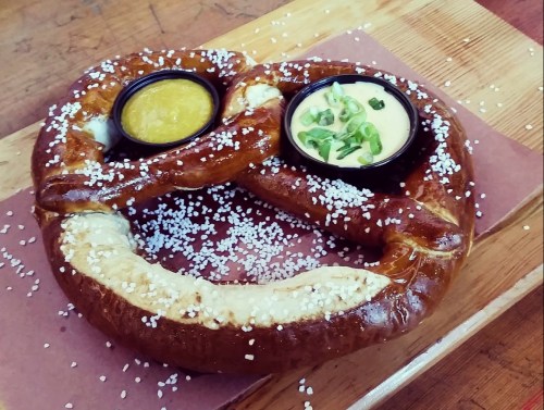 A large, soft pretzel sprinkled with coarse salt, served with two dipping sauces in small bowls.