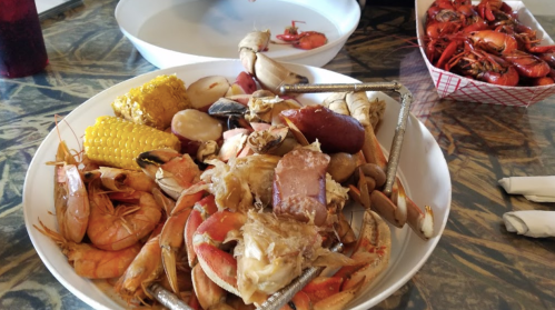 A large white bowl filled with various seafood, including shrimp, crab, corn, and potatoes, on a patterned table.