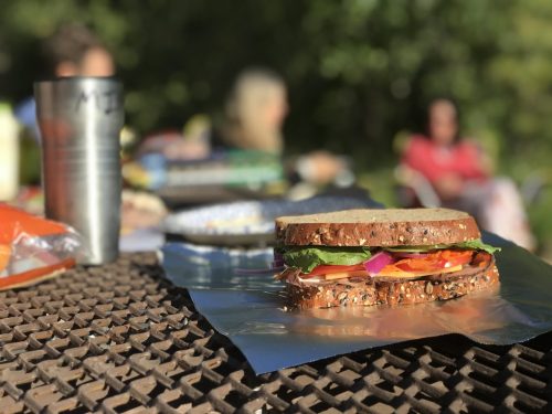 A close-up of a sandwich on a table, with a blurred background of people sitting outdoors.