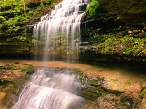 A serene waterfall cascading over rocky cliffs, surrounded by lush greenery and a tranquil pool below.