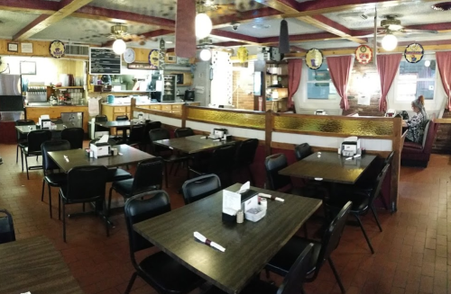 A cozy restaurant interior with empty tables, wooden decor, and a visible kitchen area in the background.
