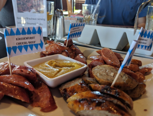 A platter of assorted sausages with labels, served with mustard in a casual dining setting.