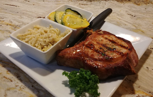 A grilled pork chop served with macaroni and cheese and sautéed zucchini and squash on a white plate.