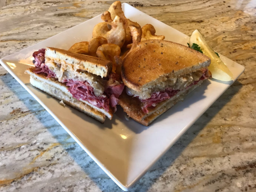 A plate with a sandwich filled with meat and cheese, accompanied by curly fries and a pickle slice.