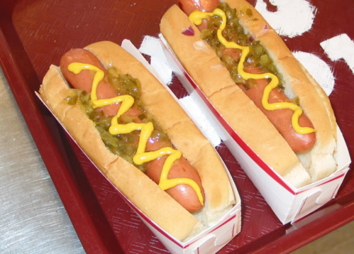 Two hot dogs in buns topped with mustard and relish, served on a red tray.