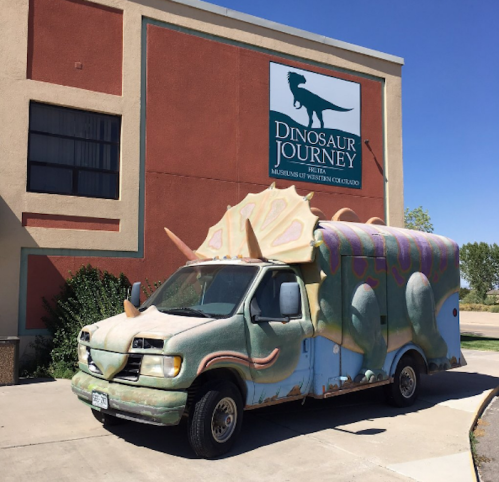 A colorful van designed to look like a triceratops parked outside the Dinosaur Journey museum in Colorado.