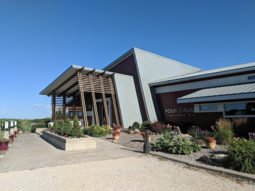 Modern winery building with a wooden facade, surrounded by colorful flowers and clear blue skies.