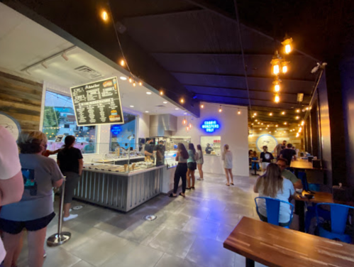 Interior of a restaurant with a menu board, customers in line, and a cozy atmosphere with string lights.