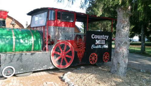 A colorful, vintage train display at Country Mill, featuring red wheels and a green engine, surrounded by trees.