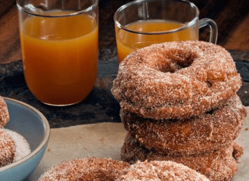A stack of cinnamon sugar donuts with two glasses of orange juice in the background.