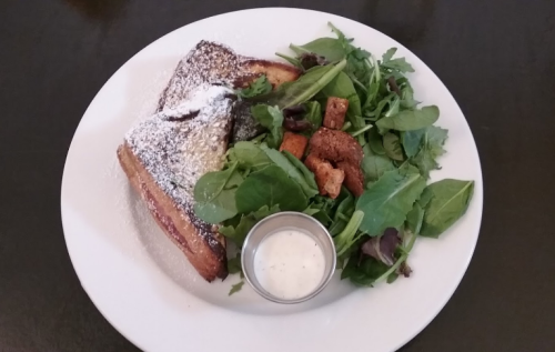 A plate featuring French toast dusted with powdered sugar, alongside a fresh green salad and a small cup of dressing.