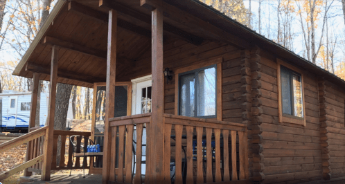 A cozy wooden cabin with a porch, surrounded by trees and autumn foliage.