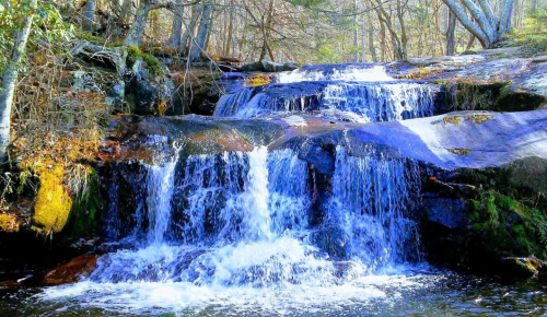 A serene waterfall cascading over rocks, surrounded by trees and natural greenery.