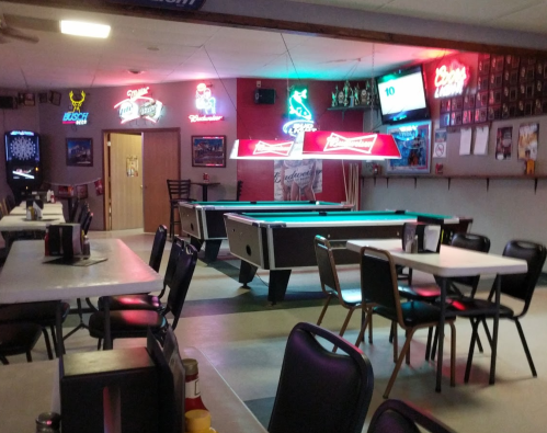A dimly lit bar with pool tables, neon signs, and empty tables set for patrons.