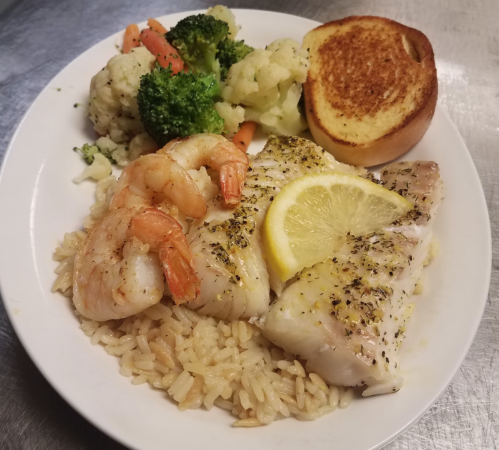 A plate of grilled fish with shrimp, lemon, rice, and a side of steamed broccoli, cauliflower, and garlic bread.