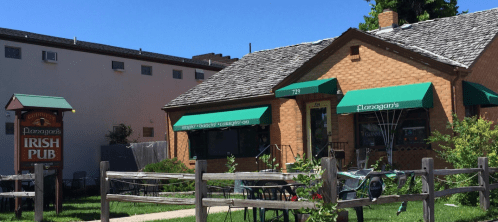 A brick building with green awnings, featuring a sign for Flanagan's Irish Pub and a fenced outdoor area.