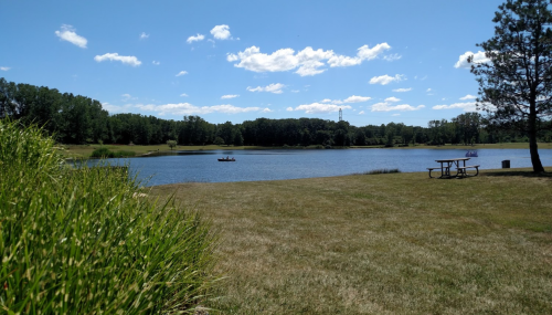 A serene lake surrounded by greenery, with a clear blue sky and a small boat in the distance.