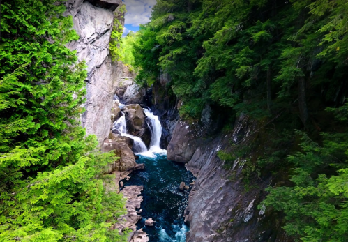 A serene waterfall cascades through rocky cliffs, surrounded by lush green trees and a clear blue river.