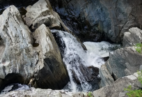 A cascading waterfall flows over large, rugged rocks in a rocky landscape.