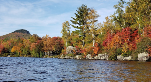 A serene lake surrounded by vibrant autumn foliage and rocky shores, with mountains in the background under a clear sky.