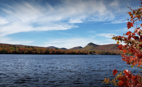 A serene lake surrounded by vibrant autumn foliage and mountains under a blue sky with wispy clouds.