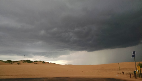 Dark storm clouds loom over a sandy landscape, with hints of rain in the distance.