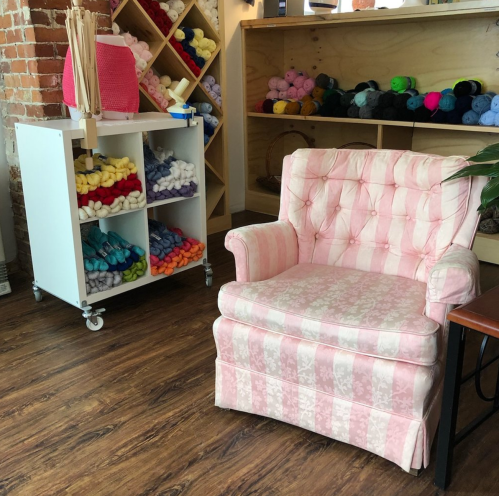 A pink tufted armchair next to a cart of colorful yarn in a cozy craft space.