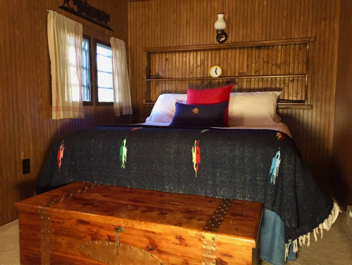 Cozy bedroom with a wooden wall, a bed with colorful blankets, and a rustic trunk at the foot.
