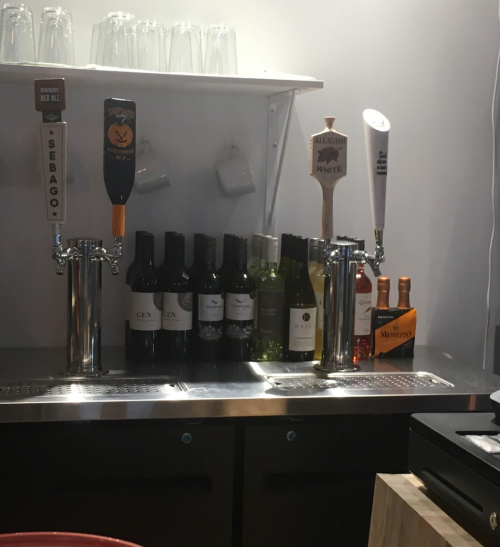 A bar counter featuring various wine bottles and beer taps, including Sebago and a pumpkin-themed tap handle.