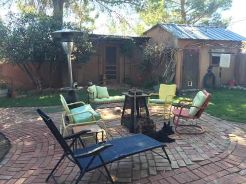 A cozy outdoor seating area with colorful chairs, a fire pit, and a patio heater surrounded by greenery.