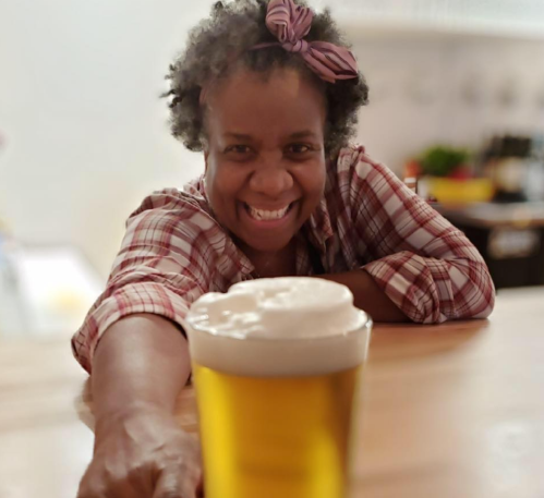 A smiling woman with curly hair reaches for a glass of beer on a bar counter.