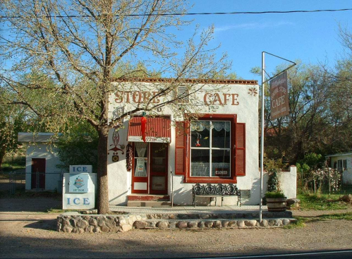 A quaint café with a red and white exterior, featuring a closed sign and an ice stand outside, surrounded by trees.