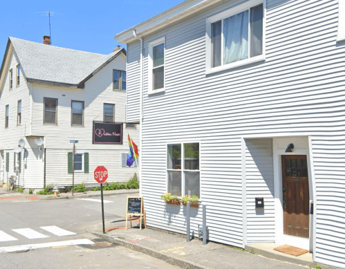 A street view of a white building with a sign reading "Love Nest," featuring a rainbow flag and a stop sign nearby.