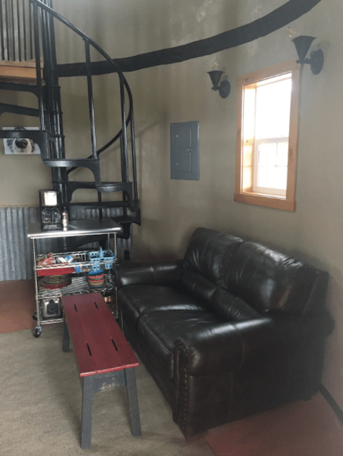 Cozy interior with a spiral staircase, leather couch, red coffee table, and a window letting in natural light.
