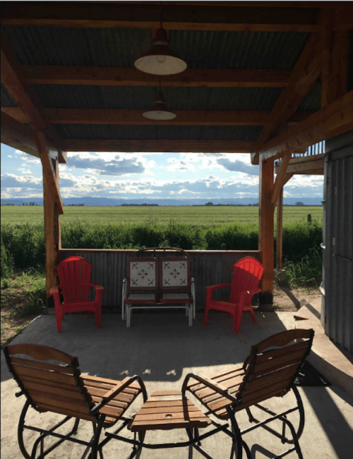 A cozy outdoor seating area with red and wooden chairs, overlooking a green field and blue sky with clouds.