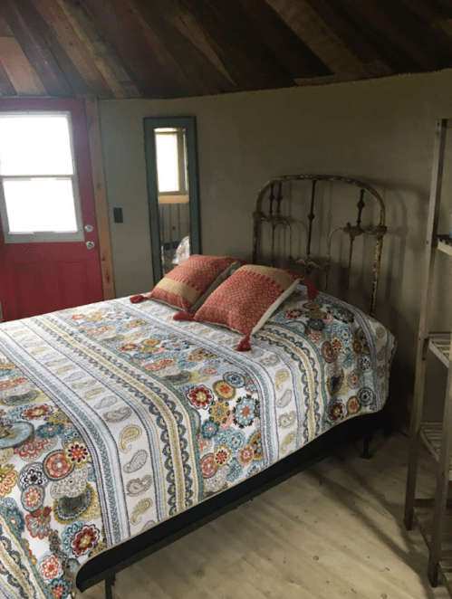 Cozy bedroom with a patterned quilt, two pillows, and a rustic metal bed frame, featuring a red door and mirror.