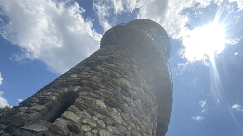 A tall stone tower under a bright sky with fluffy clouds and sunlight shining from the top.