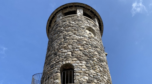 A tall stone tower with a circular design, featuring a balcony and set against a clear blue sky.