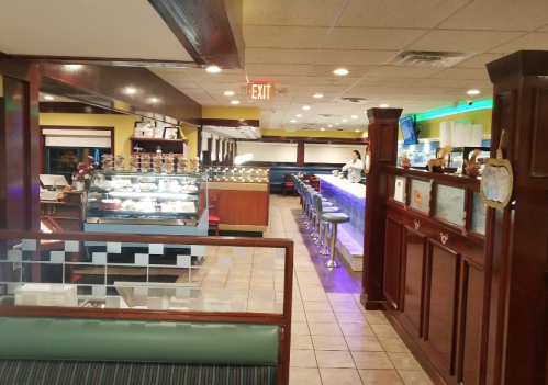 Interior of a diner featuring a dessert display, bar seating, and a brightly lit counter area.