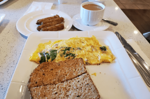 A plate with an omelette, two sausage links, and two slices of whole grain toast, alongside a cup of coffee.
