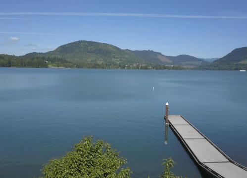 A serene lake view with a wooden dock, surrounded by green hills under a clear blue sky.