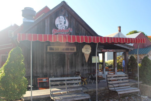 A rustic wooden building with a red and white striped awning, featuring a sign that reads "Mildred's" and outdoor seating.