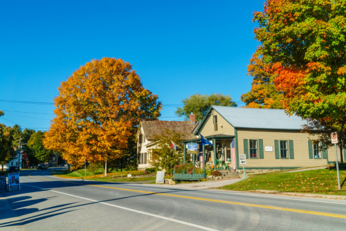 A quaint house on a sunny street, surrounded by vibrant autumn trees and a clear blue sky.